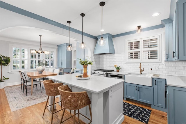 kitchen featuring light countertops, light wood-style flooring, stainless steel stove, custom exhaust hood, and a sink