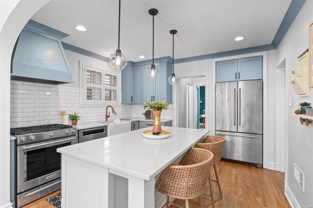 kitchen with blue cabinets, visible vents, light wood-style flooring, custom range hood, and stainless steel appliances