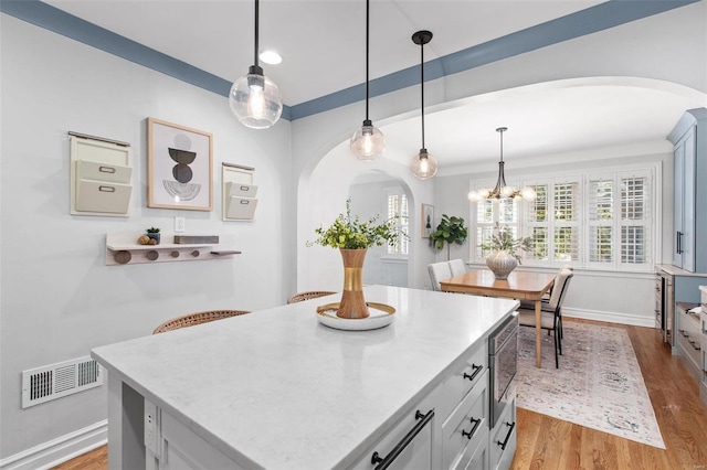 kitchen featuring arched walkways, visible vents, decorative light fixtures, and wood finished floors