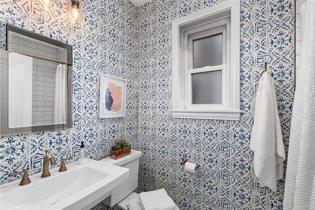 bathroom with toilet, wallpapered walls, and a sink