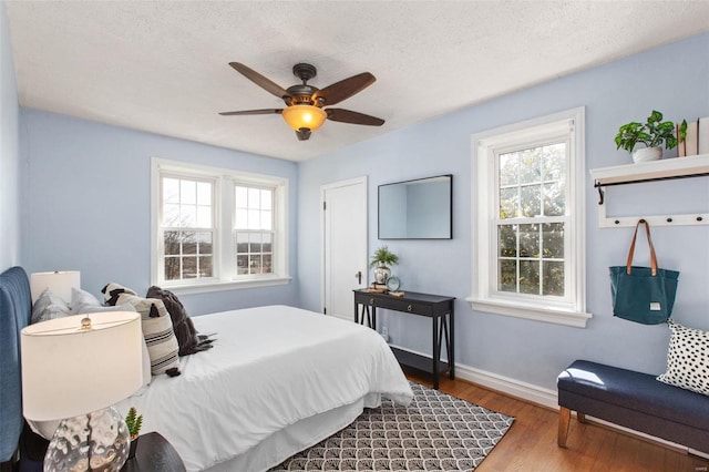 bedroom with multiple windows, wood finished floors, baseboards, and a textured ceiling