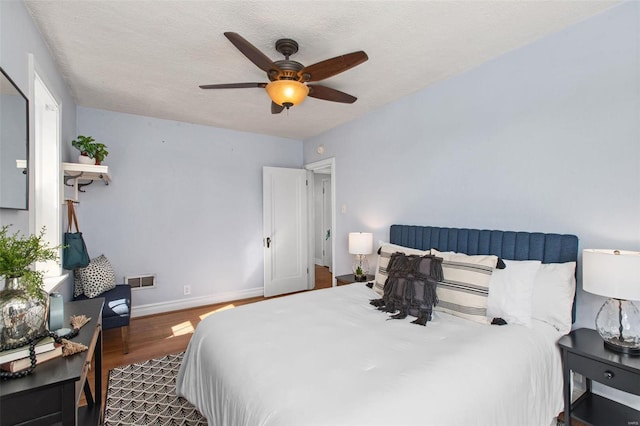 bedroom featuring a ceiling fan, baseboards, wood finished floors, visible vents, and a textured ceiling