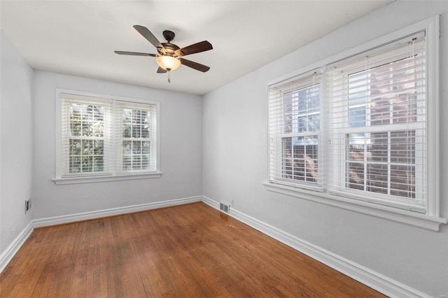 empty room with visible vents, a ceiling fan, baseboards, and wood finished floors