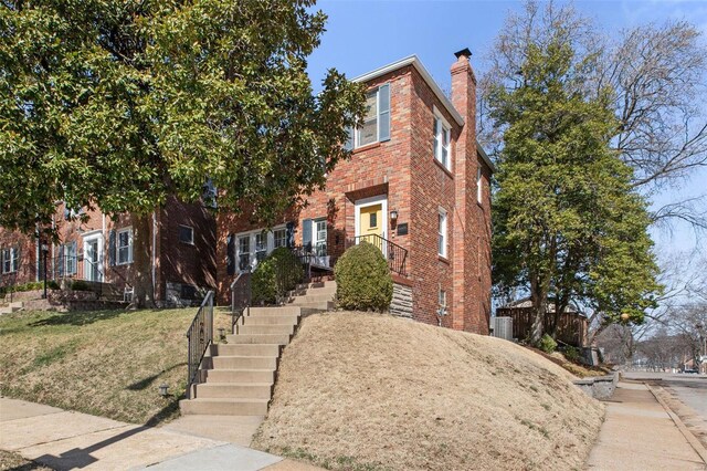 view of front of home featuring brick siding, a chimney, and a front yard