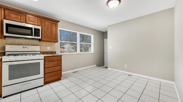 kitchen featuring tasteful backsplash, stainless steel microwave, brown cabinetry, white range with gas cooktop, and baseboards