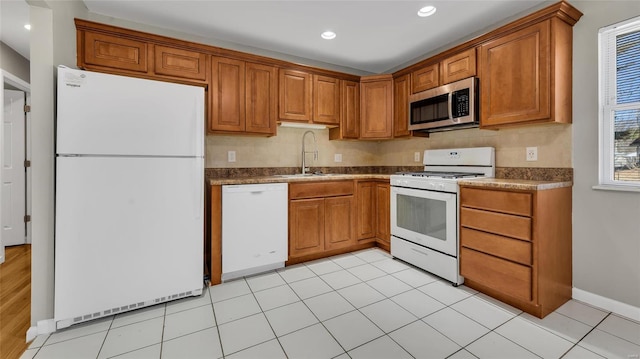 kitchen with white appliances, brown cabinetry, dark countertops, and a sink