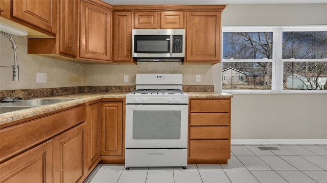 kitchen featuring a sink, stainless steel microwave, brown cabinets, and white range with gas stovetop