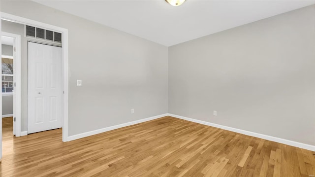 spare room with light wood-type flooring, visible vents, and baseboards