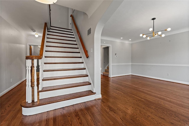 stairway featuring baseboards, visible vents, arched walkways, wood finished floors, and a chandelier