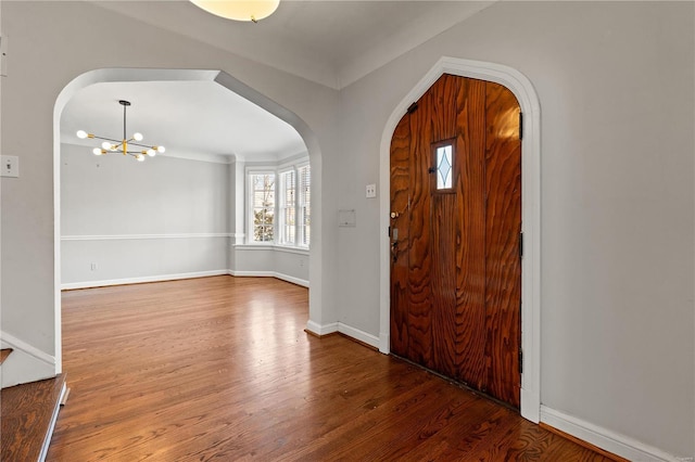 foyer with a chandelier, arched walkways, baseboards, and wood finished floors