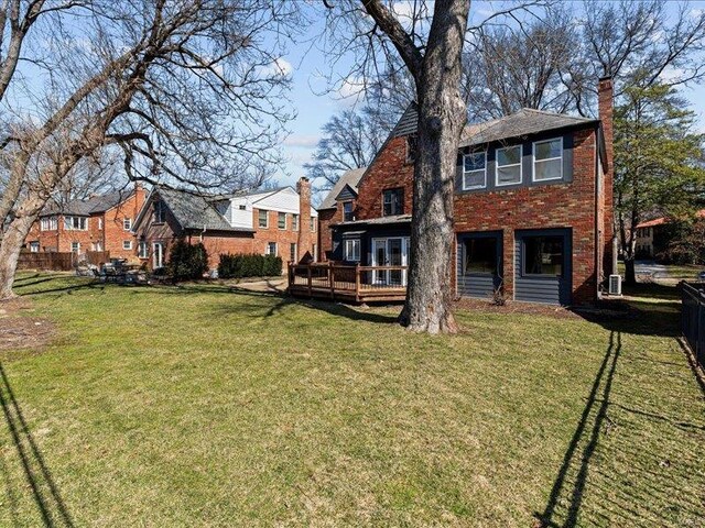 back of house featuring a chimney, fence, a deck, and a lawn