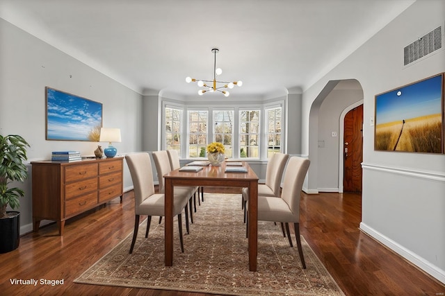 dining area featuring dark wood-style floors, baseboards, arched walkways, and a notable chandelier