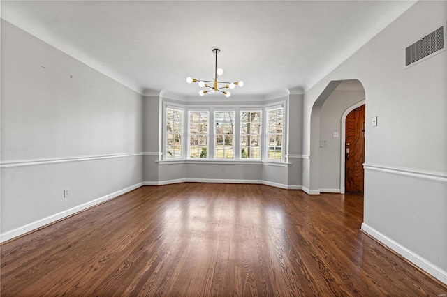 spare room with a notable chandelier, baseboards, arched walkways, and wood finished floors