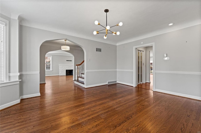 empty room with visible vents, a fireplace, baseboards, and wood finished floors