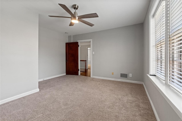 carpeted empty room with a ceiling fan, visible vents, and baseboards