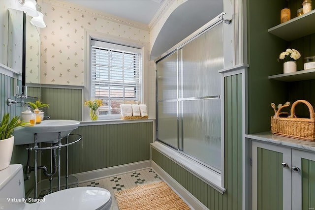 full bath featuring toilet, a wainscoted wall, bath / shower combo with glass door, tile patterned floors, and wallpapered walls