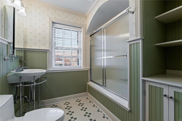 bathroom with toilet, wallpapered walls, enclosed tub / shower combo, and a wainscoted wall