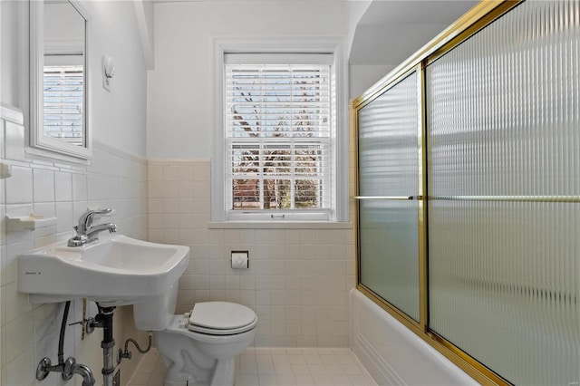 bathroom featuring enclosed tub / shower combo, tile patterned flooring, toilet, tile walls, and wainscoting