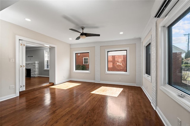 empty room featuring an AC wall unit, baseboards, dark wood-type flooring, and a stone fireplace