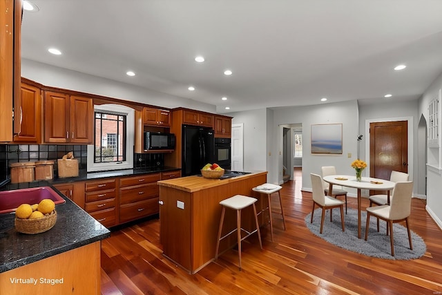 kitchen with tasteful backsplash, dark wood finished floors, a center island, black appliances, and a kitchen bar