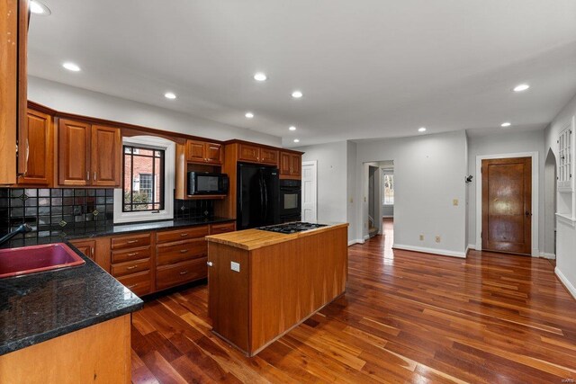 kitchen featuring dark wood-type flooring, a kitchen island, a sink, black appliances, and tasteful backsplash