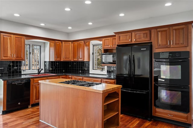 kitchen with a kitchen island, a sink, black appliances, and wood finished floors