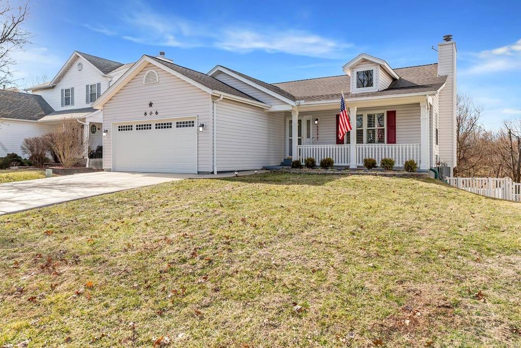 view of front of property featuring an attached garage, covered porch, concrete driveway, a front lawn, and a chimney