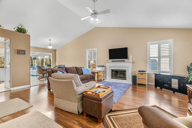 living area featuring lofted ceiling, wood finished floors, a ceiling fan, baseboards, and a glass covered fireplace