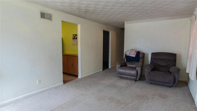 living area with light carpet, a textured ceiling, visible vents, and baseboards