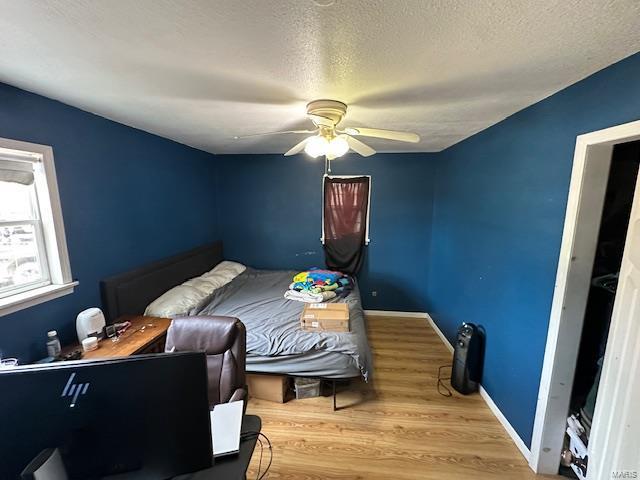 bedroom with ceiling fan, a textured ceiling, baseboards, and wood finished floors