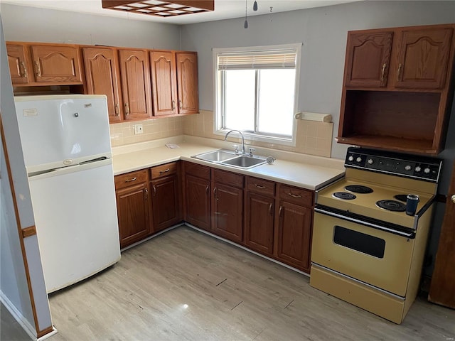 kitchen featuring freestanding refrigerator, a sink, light wood-style floors, backsplash, and range with electric stovetop