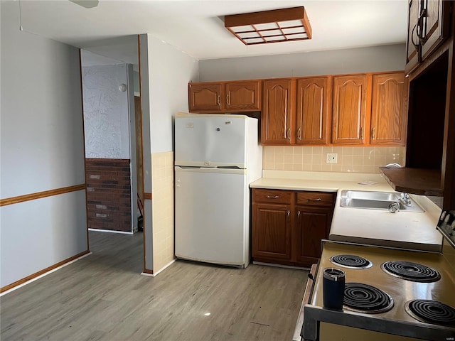 kitchen featuring light wood finished floors, electric range oven, a wainscoted wall, freestanding refrigerator, and light countertops