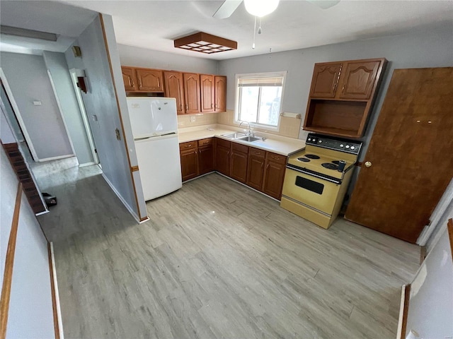 kitchen with light wood finished floors, electric range oven, freestanding refrigerator, light countertops, and a sink