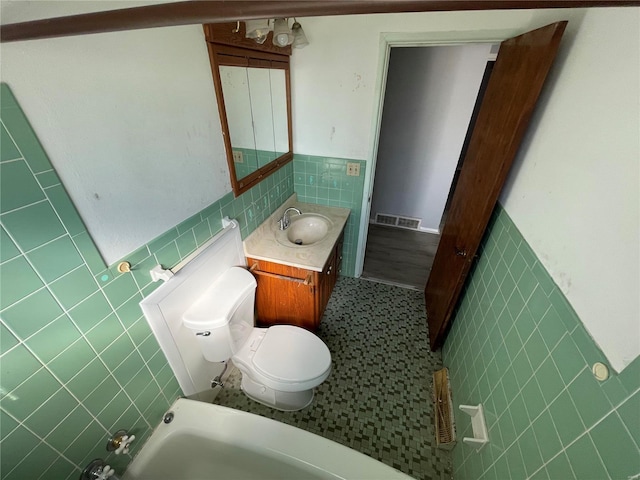 bathroom featuring visible vents, toilet, a wainscoted wall, vanity, and tile walls