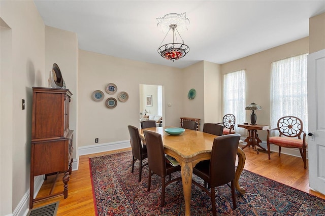 dining space with light wood-type flooring, visible vents, and baseboards