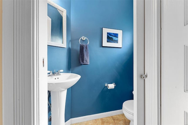 half bath featuring tile patterned floors, a sink, toilet, and baseboards