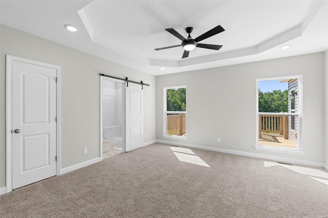 unfurnished bedroom with a raised ceiling, multiple windows, baseboards, and a barn door