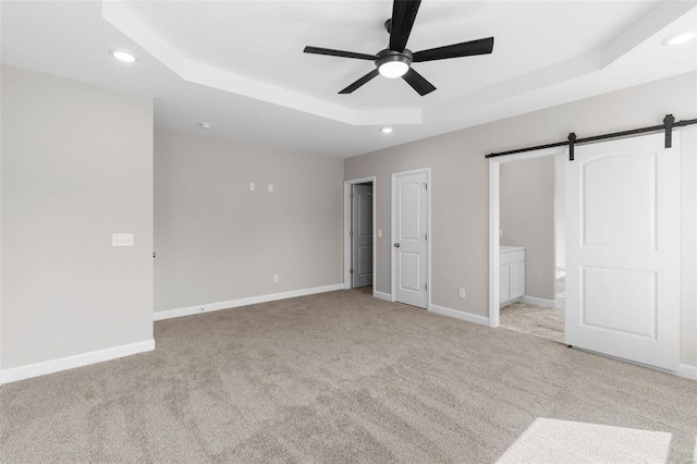 unfurnished bedroom featuring a barn door, baseboards, a raised ceiling, carpet, and recessed lighting