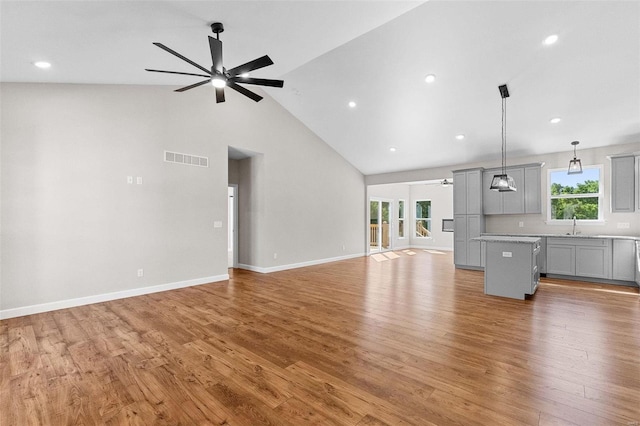 unfurnished living room with baseboards, visible vents, a ceiling fan, light wood-style floors, and high vaulted ceiling