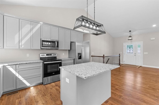 kitchen featuring appliances with stainless steel finishes, vaulted ceiling, a kitchen island, and light wood finished floors