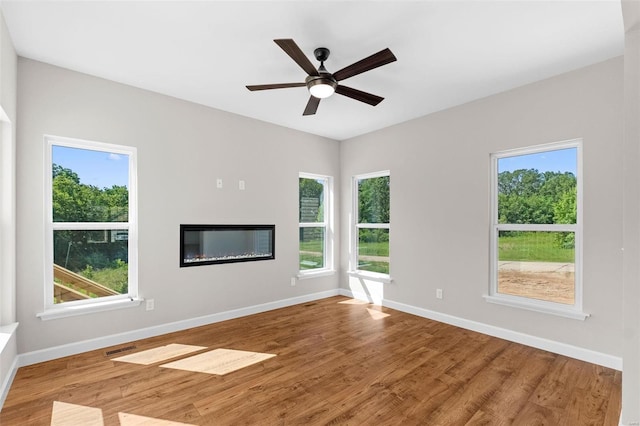 unfurnished living room featuring baseboards, wood finished floors, and a glass covered fireplace