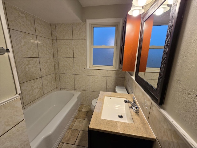 bathroom with a bathing tub, toilet, vanity, tile walls, and tile patterned floors