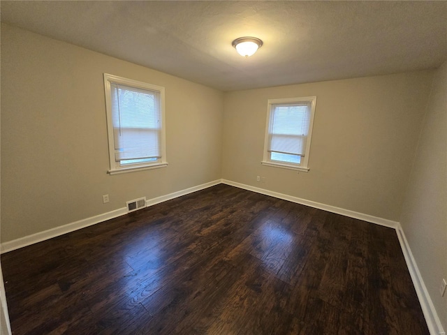 empty room with dark wood-style floors, visible vents, and baseboards