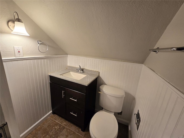 half bathroom with a textured ceiling, vaulted ceiling, vanity, and toilet