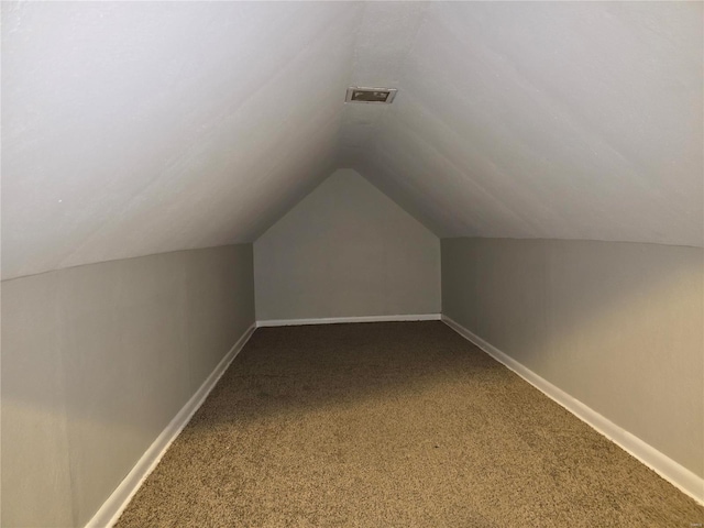 additional living space featuring lofted ceiling, visible vents, dark carpet, and baseboards