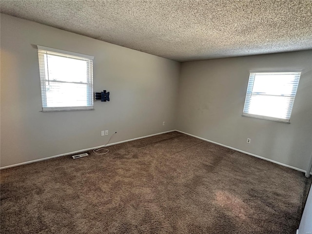 unfurnished room featuring a healthy amount of sunlight, carpet floors, visible vents, and a textured ceiling