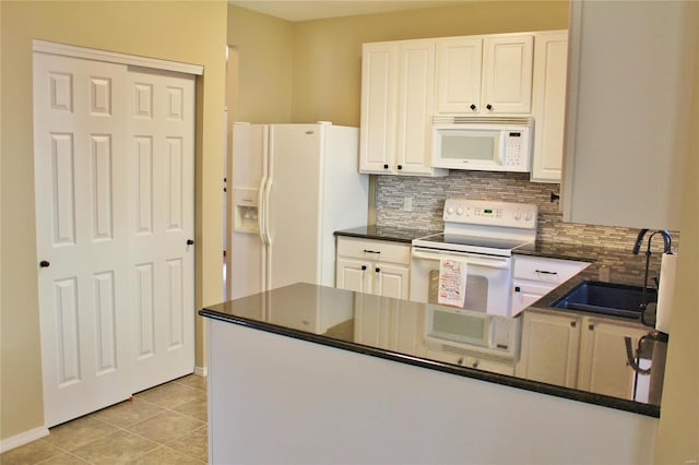 kitchen featuring white appliances, dark countertops, a peninsula, a sink, and light tile patterned flooring