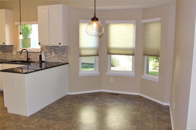 kitchen with tasteful backsplash, dark countertops, hanging light fixtures, white cabinetry, and a sink