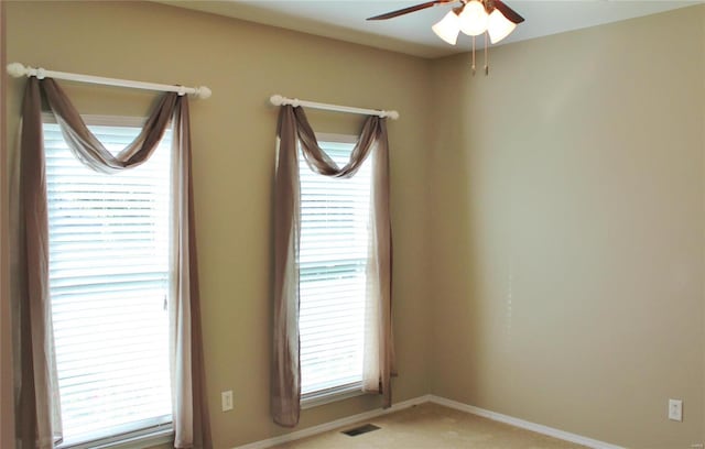 spare room featuring a ceiling fan, light colored carpet, visible vents, and baseboards