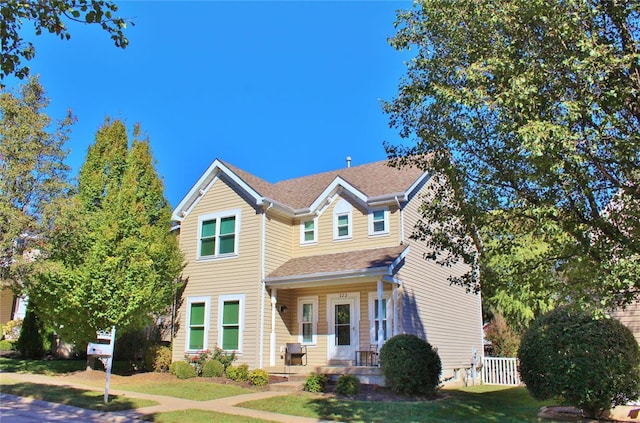 traditional home featuring a porch, fence, and a front lawn